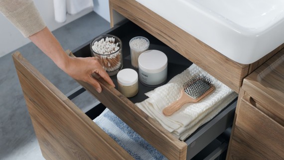 A hand opens one of the drawers of the Geberit Selnova washbasin cabinet in a natural design